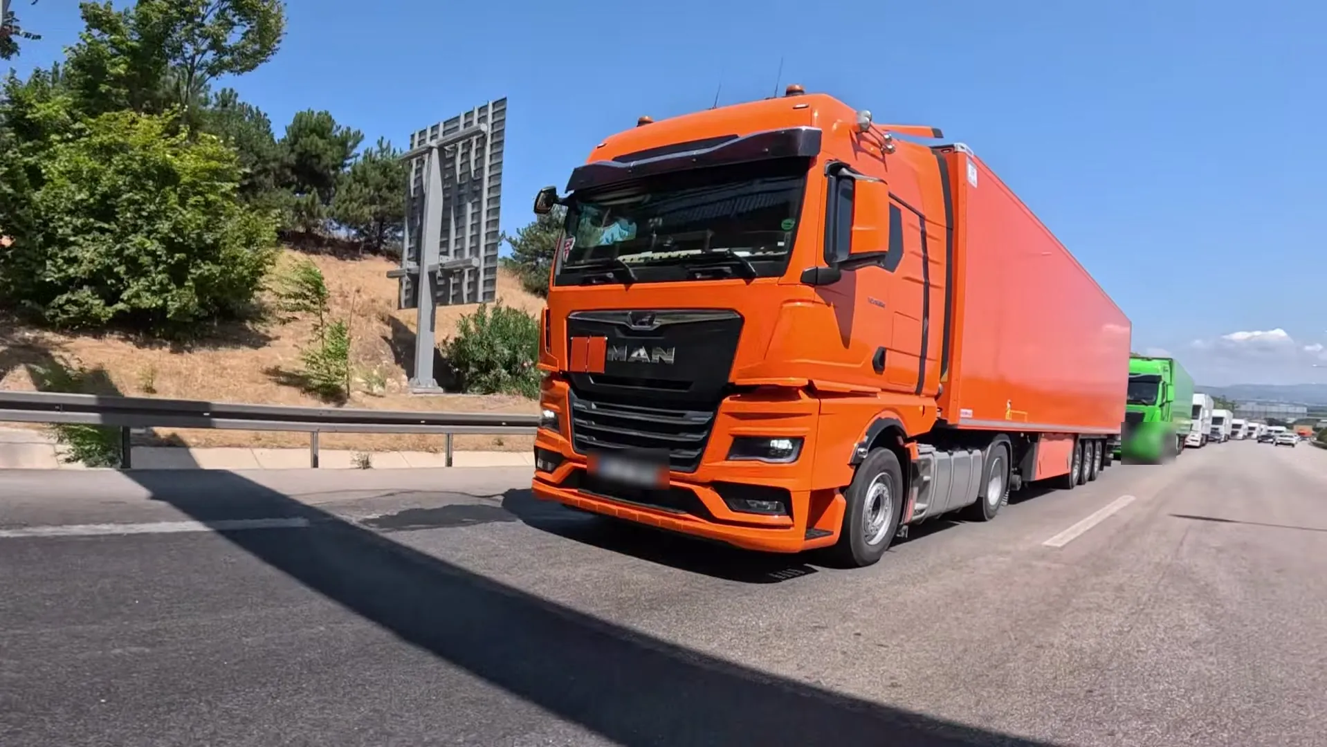 Orangefarbene MAN-TGX-Zugmaschine auf der Autobahn, dahinter ein Lkw-Konvoi